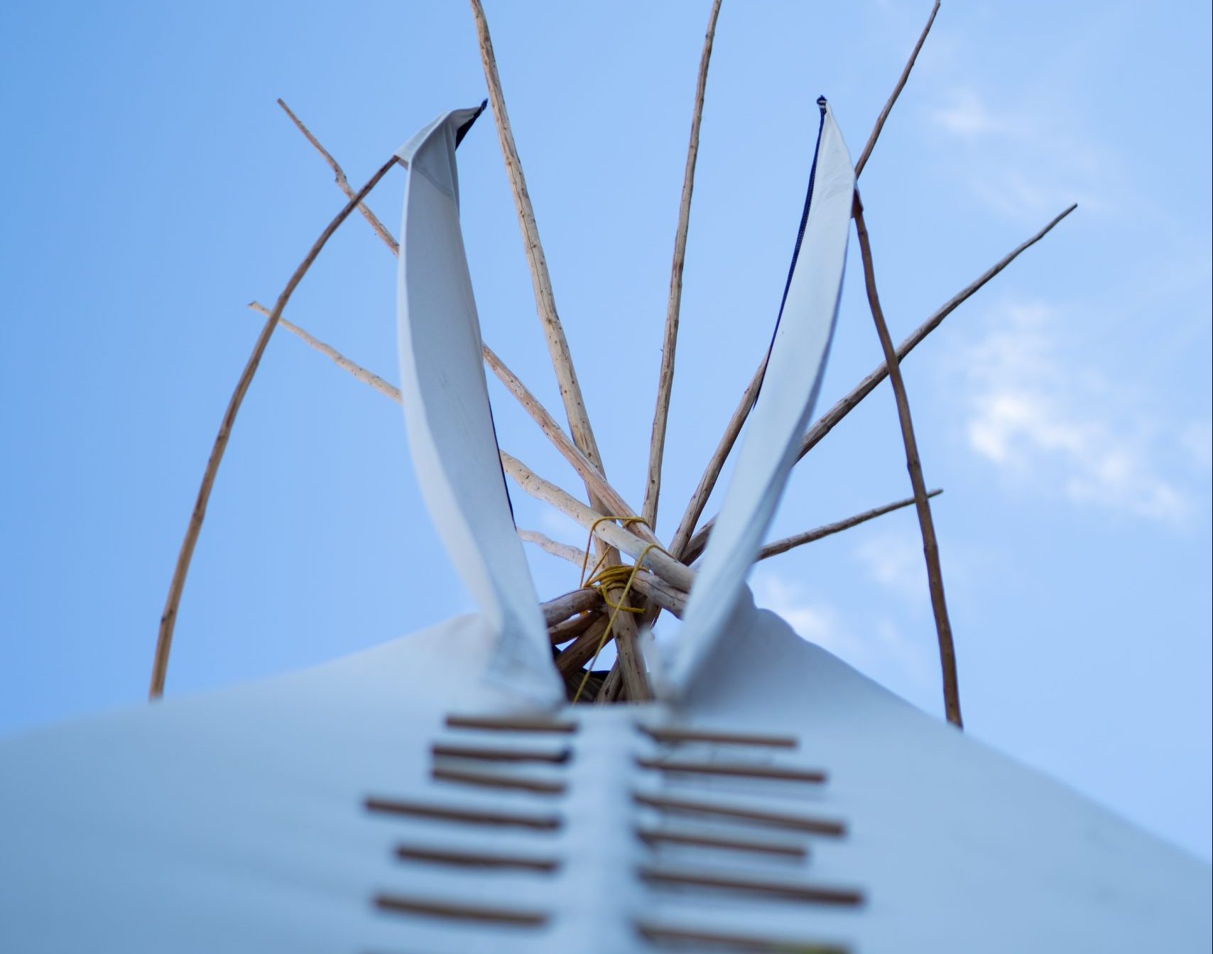 A photo of a tipi, shot at an upwards angle with a blue sky in the background.