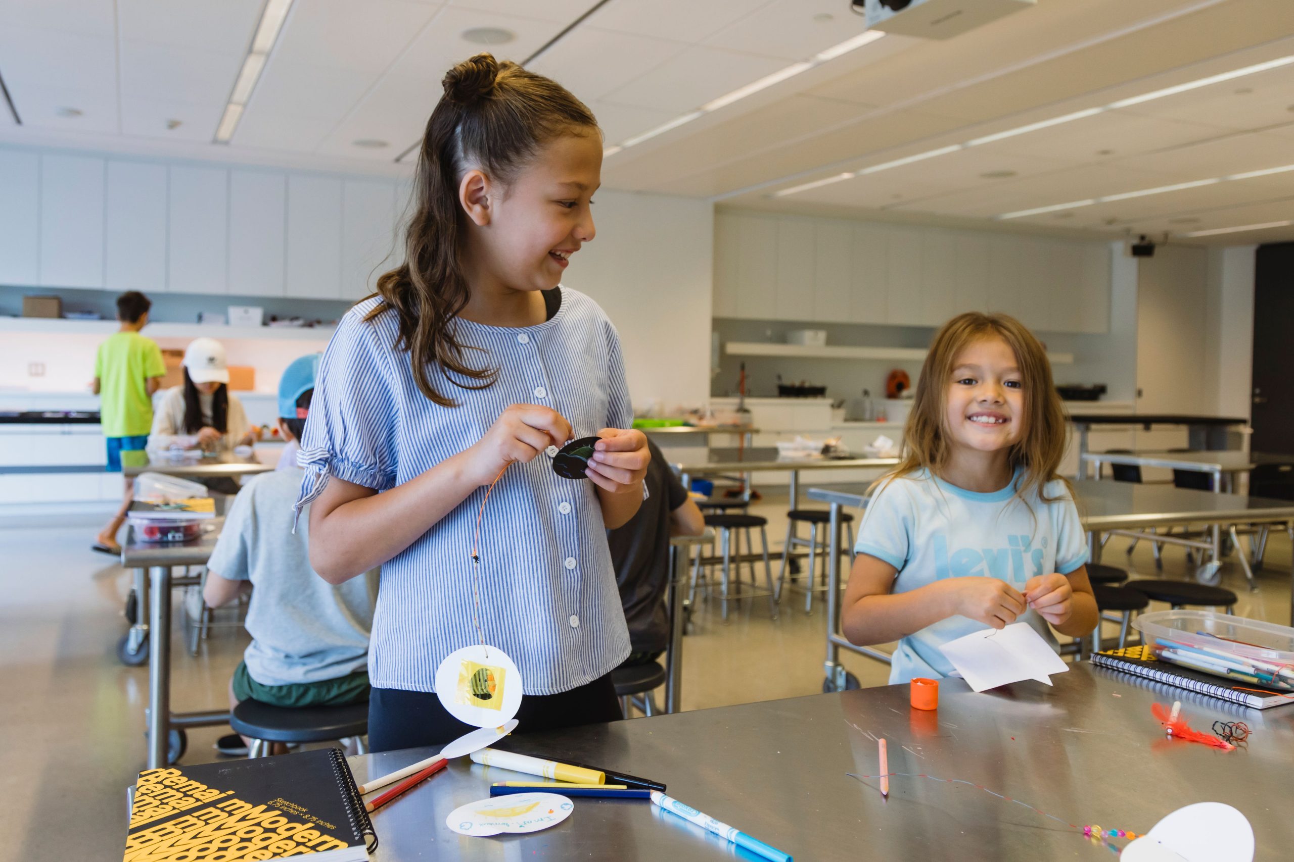 Two children smile at one another as they make art in Remai Modern's learning studio.