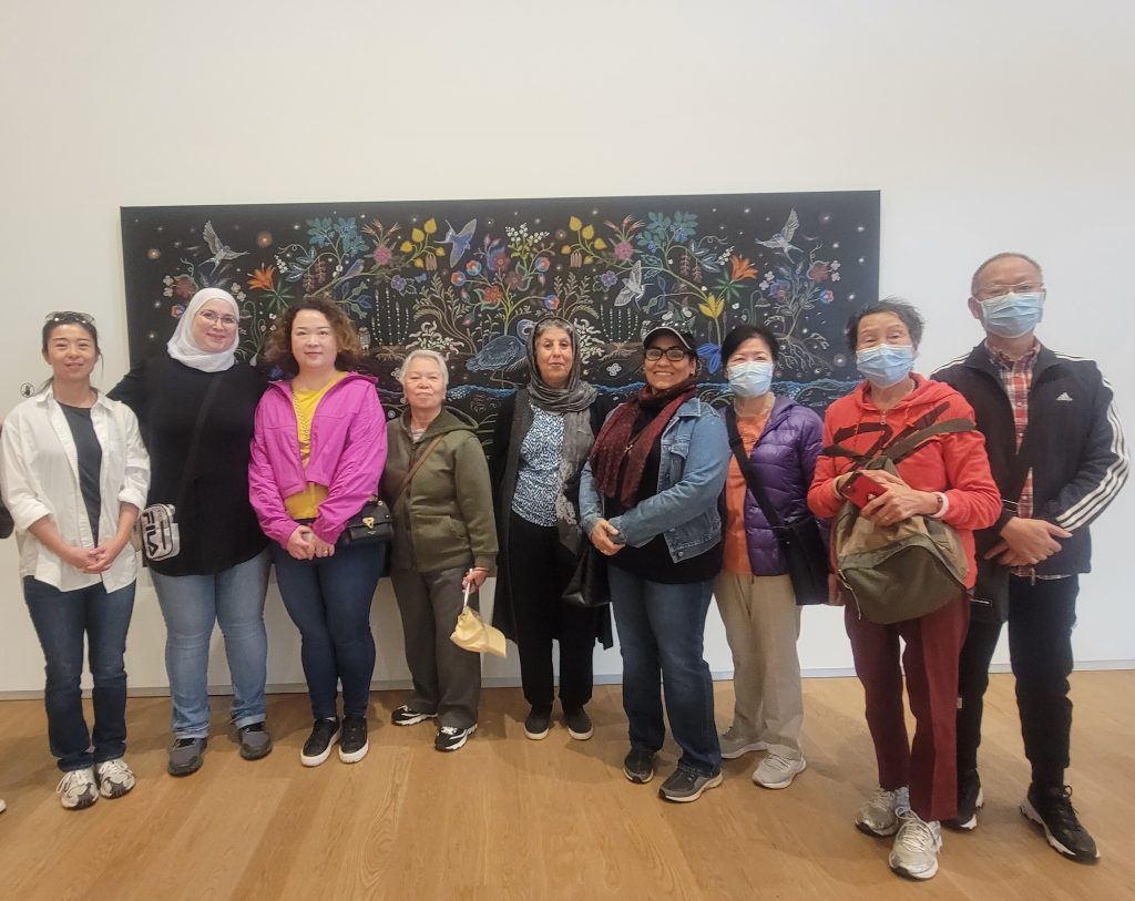 A group of newcomers pose for a picture in front of a painting at Remai Modern.