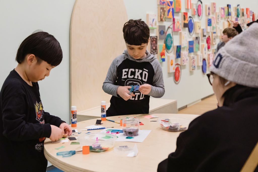 Children make art collages together at a table in the exhibition All Aboard: Everyone an Artist.