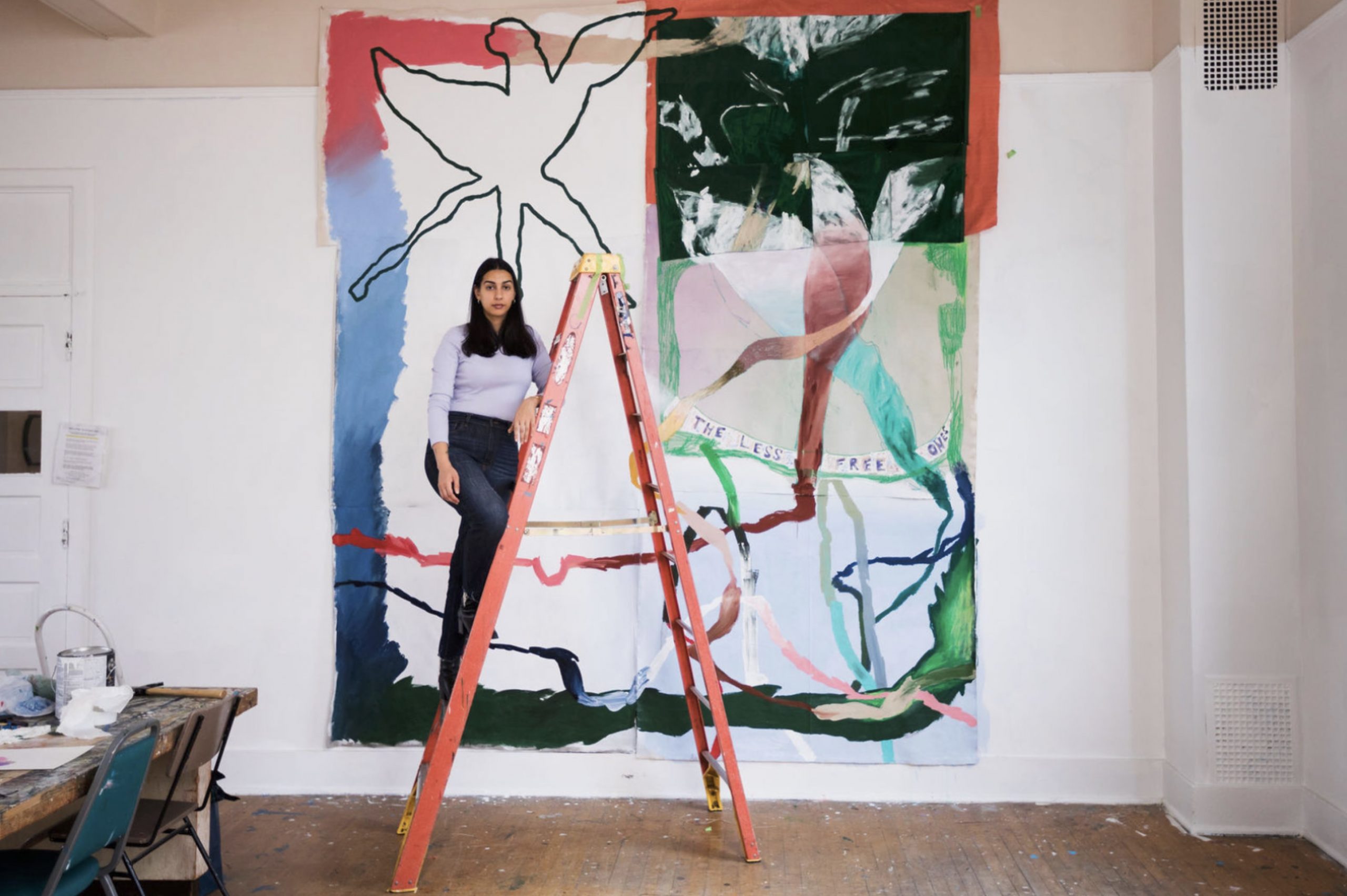 Artist Russna Kaur on a ladder in front of a painting