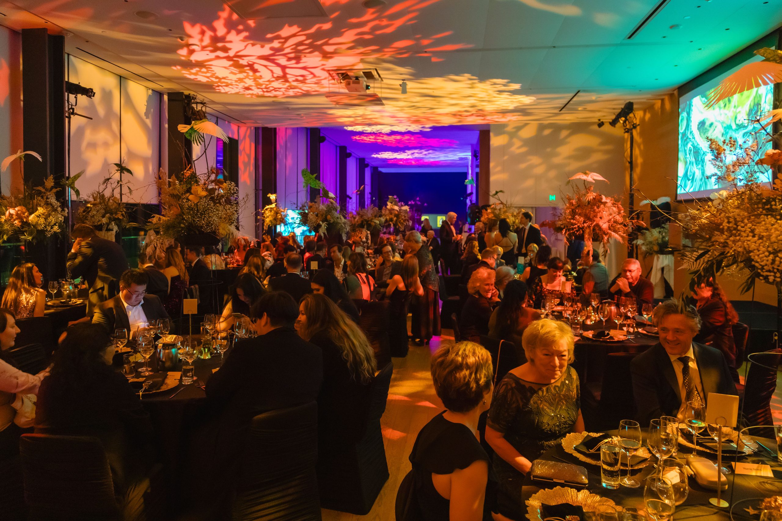 Guests dine together at Remai Modern's galaMODERN fundraiser. The room is filled with vibrant lighting and decor.