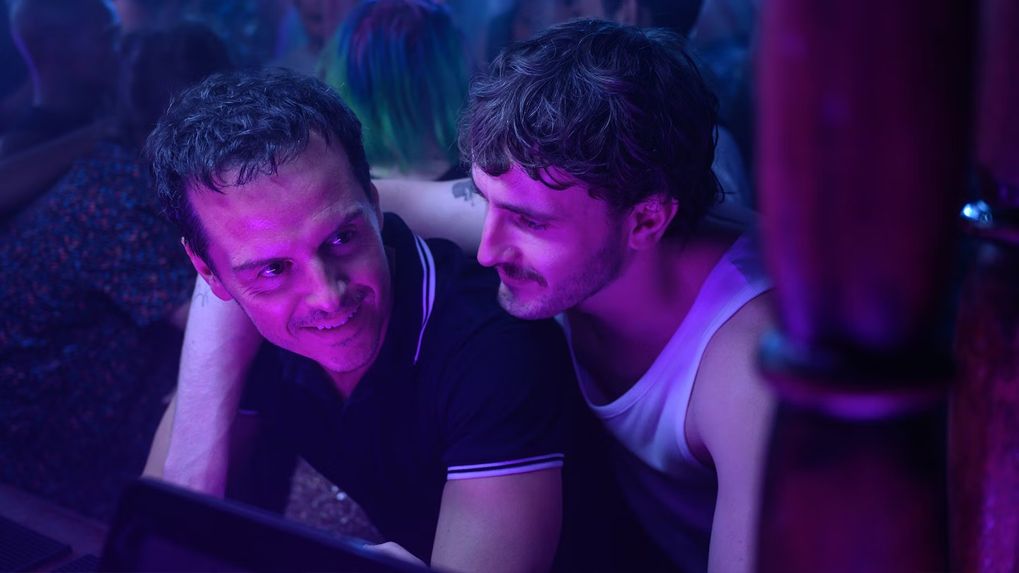 Two men stand together at a club, one with his arm around the other.