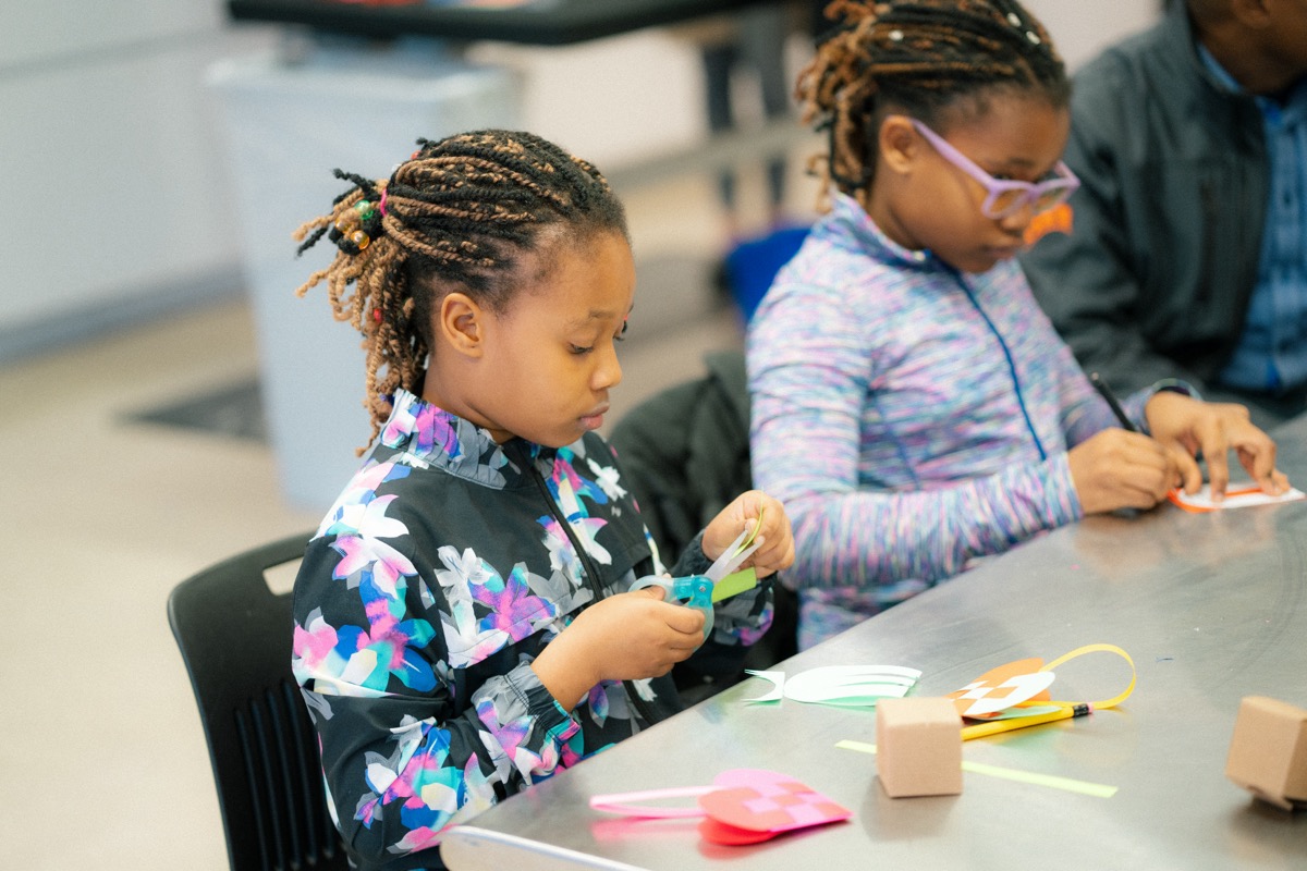 Children engaged in creative activities at a table, using colorful paper and scissors to craft intricate designs, in a bright, collaborative environment.