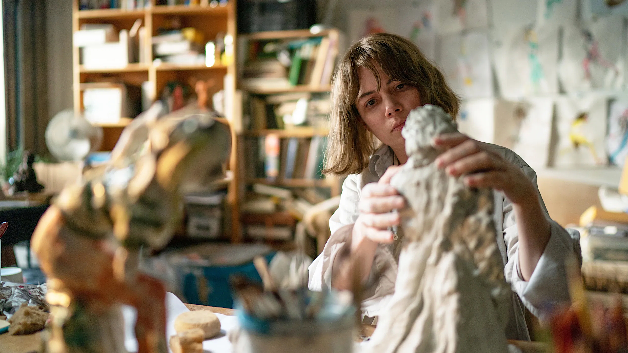 A woman skillfully creates a sculpture in her art studio, surrounded by tools and materials for her craft.