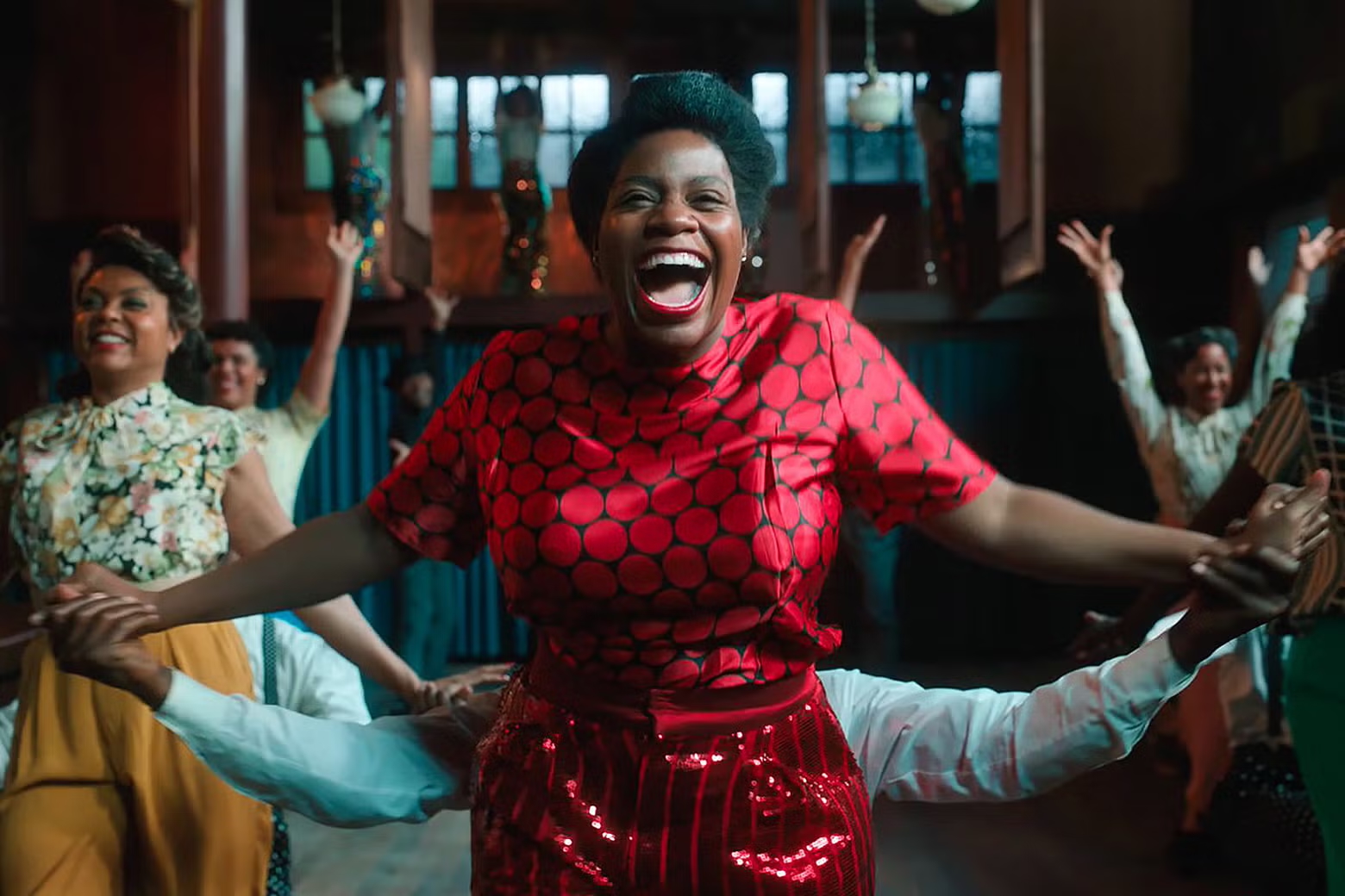 A woman in a red dress dances joyfully among a group of people, showcasing vibrant movement and celebration.