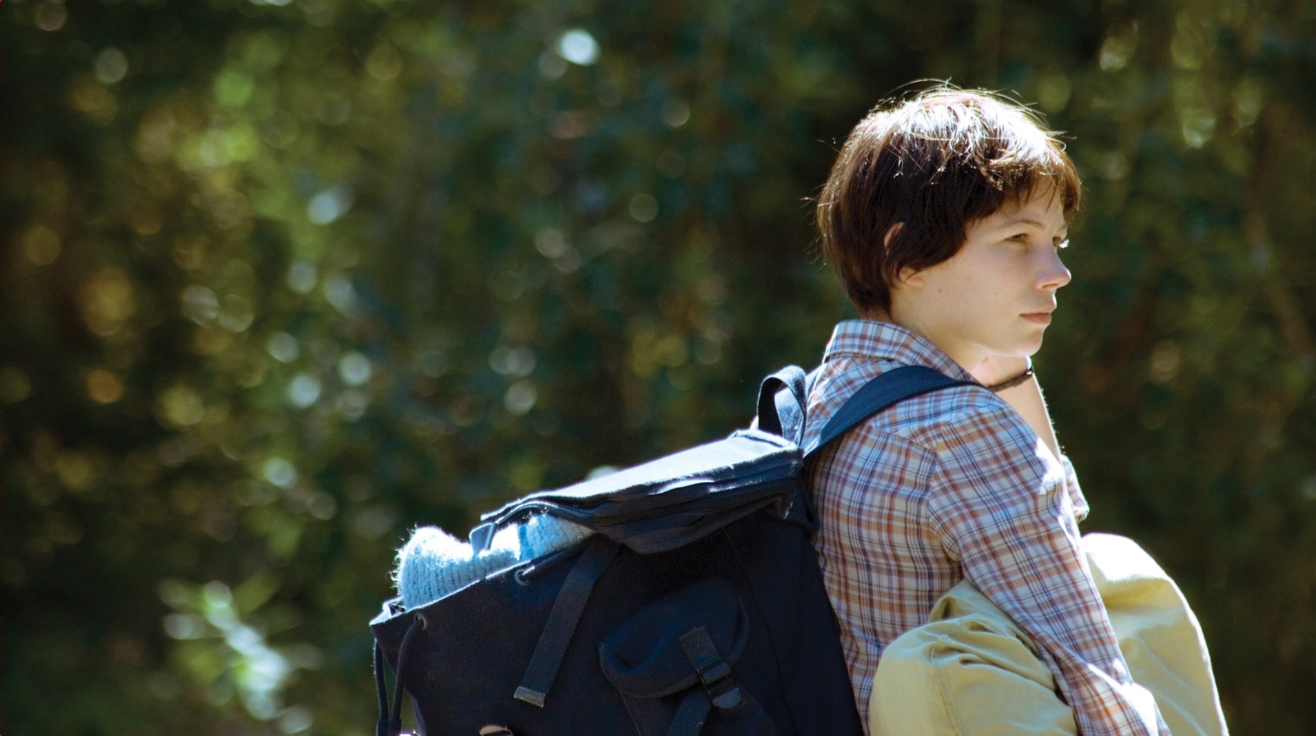 A young person carrying a backpack strolls along a scenic path surrounded by greenery.