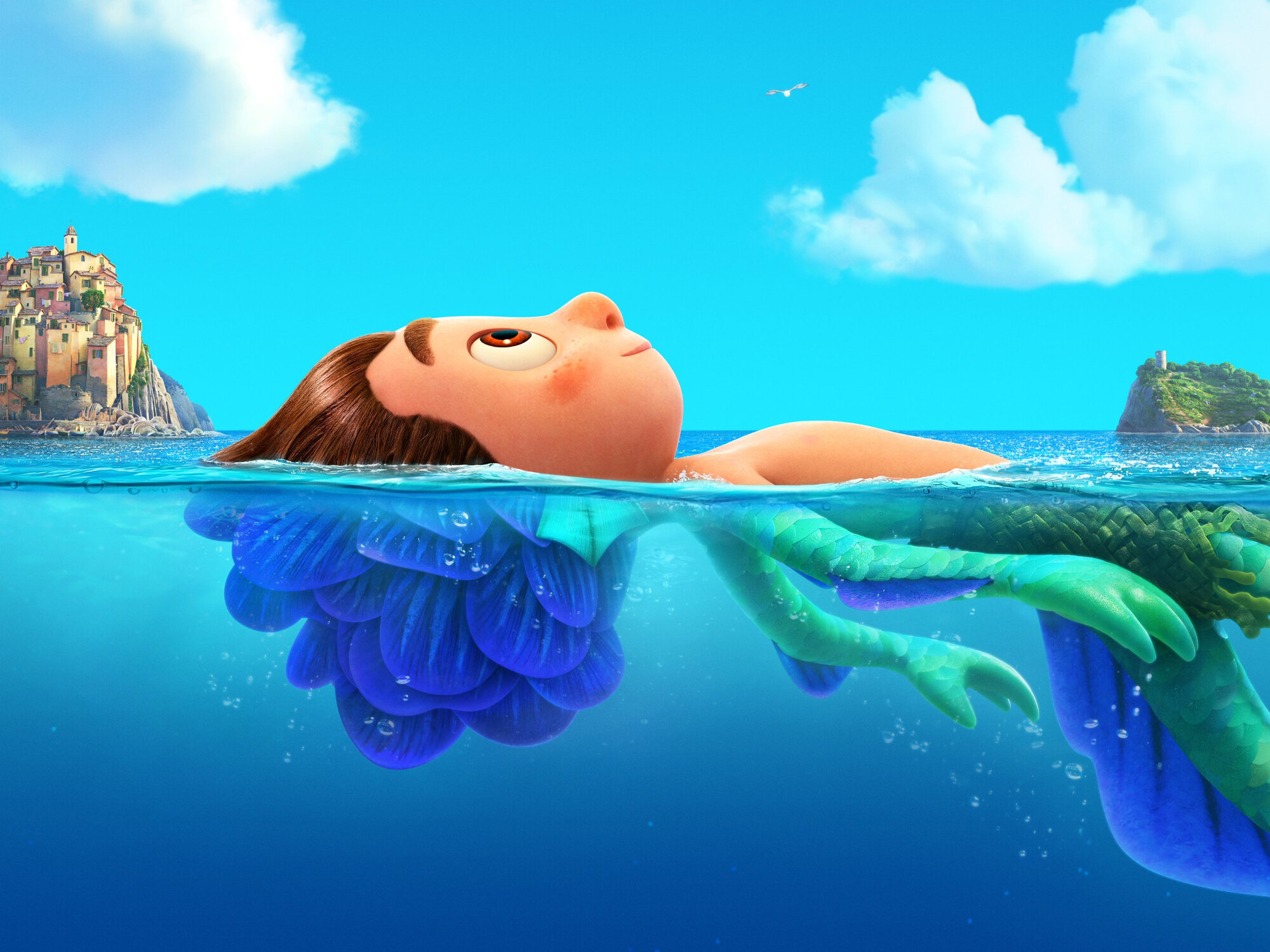 An animated boy with brown hair floats on his back in bright blue ocean water. Above the surface, he looks human with a relaxed expression. Below the surface, his body transforms into a colorful sea creature with green scaled limbs and a purple tail. In the distance, a small coastal village sits on rocky cliffs under a sunny sky with fluffy clouds.